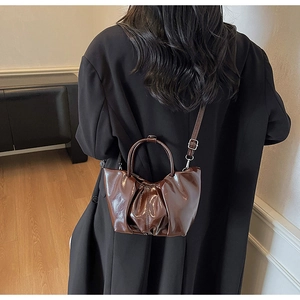 Detail of dark brown glossy pleated handbag with circular handle and cross-body strap