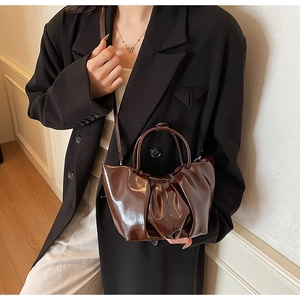 Deep brown glossy patent leather cloud bag featuring pleated texture and top handle