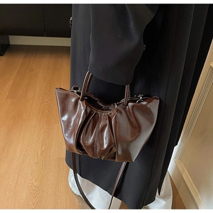 Detail of a deep brown pleated handbag featuring glossy oil wax leather and slim handles