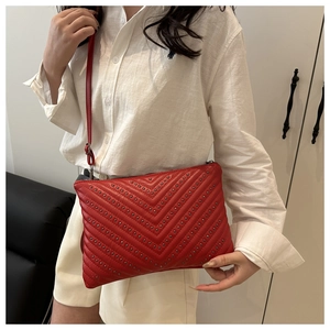 Detail of red quilted clutch bag with metallic studs and slender leather shoulder strap