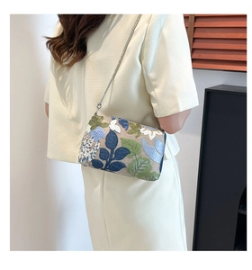 Detail of floral embroidery and sequins on a cream crossbody bag with silver chain