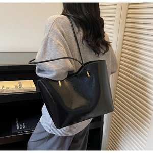 Detail of glossy black patent leather tote bag with wavy edges and gold metallic hardware
