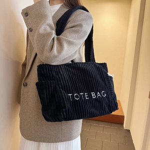 Minimalist black corduroy tote bag with TOTE BAG embroidery shown on shoulder