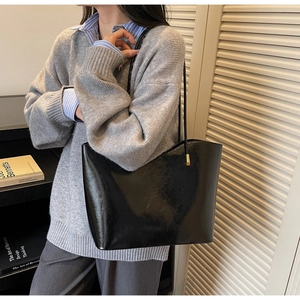 Detail of black glossy tote bag with fine leather texture and golden metal accents
