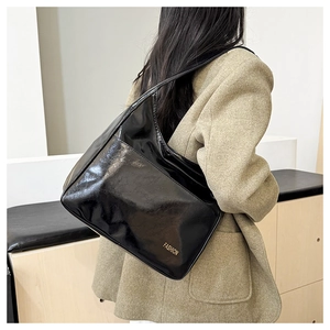 Close-up of black glossy patent leather shoulder bag with golden fashion logo lettering
