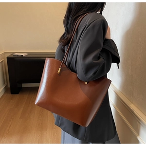 Detail of a large brown glossy leather tote bag with elegant gold metal buckles