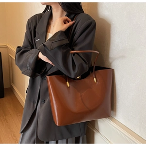 Detail of a deep brown shiny leather tote bag with thin round straps and gold hardware