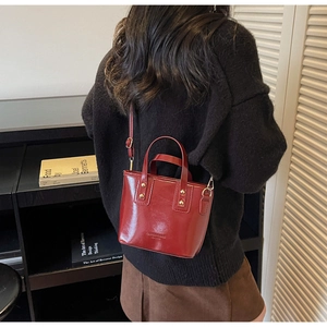 Détail macro du sac seau en cuir verni rouge foncé avec rivets dorés et anses