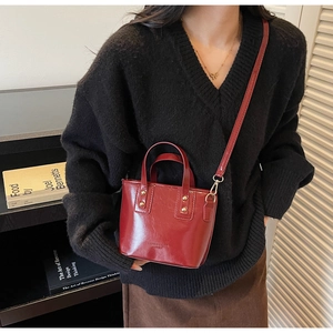 Detail of red glossy patent leather handbag with gold rivets and detachable strap
