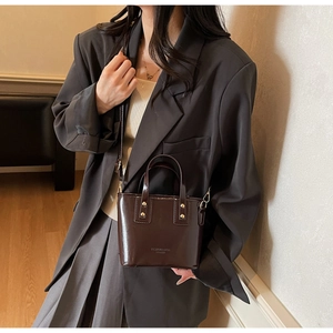 Détail du sac seau en cuir verni marron foncé avec poignée et rivets dorés