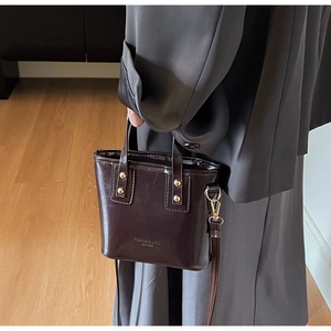 Vue détaillée du sac seau en cuir verni marron foncé avec rivets dorés et logo