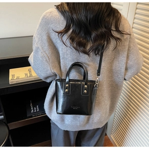 Modèle portant un sac seau en cuir verni noir avec détails dorés et bandoulière fine