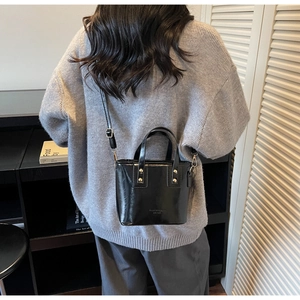 Detail of black glossy patent leather mini bucket bag with gold studs and shoulder strap