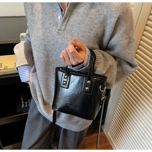 Detail of black glossy mini bucket bag featuring gold rivets and crossbody metal rings