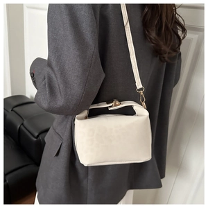 Detail of creamy white pillow bag with embossed animal texture on a model in a grey suit