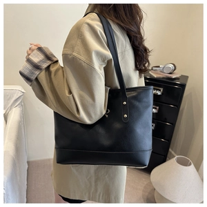 Detail of black leather tote bag featuring gold rivet accents on the shoulder strap