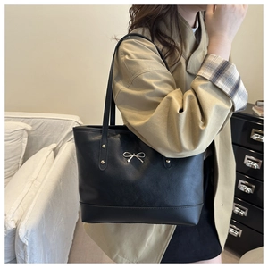 Shoulder shot of a matte black tote bag with silver bow accent and large interior