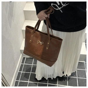 Detail of a brown tote bag with gold bow ornament and rivets for elegant women's fashion
