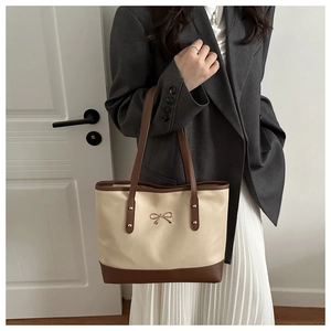 Detailed shot of beige and brown tote bag with golden bow ornament on model