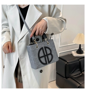 Detail of grey felt tote bag featuring black AB patch and golden ring hardware accents