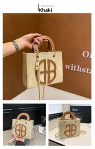 Detail view of khaki tote bag featuring brown leather trim and golden hardware buckles