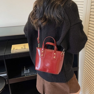 Sac seau bordeaux brillant avec détails dorés porté par un mannequin de profil