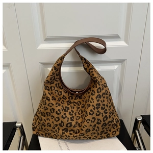 Detail view of large leopard print tote bag with brown leather straps on a black chair