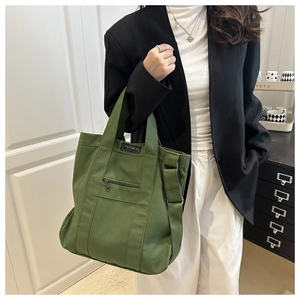 Detail of green canvas tote showing the adjustable strap and fashion label on the front