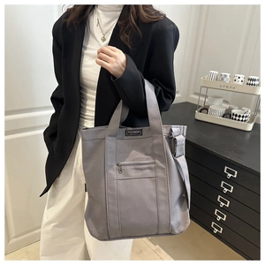 Detailed close-up of a large grey canvas tote bag featuring a front zipper and Fashion label