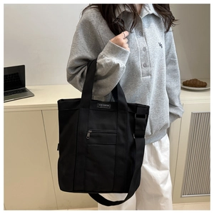 Detail view of large black canvas tote bag featuring adjustable strap and fashion label