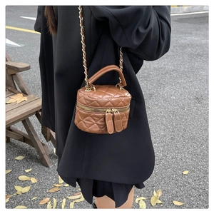 Detail of a brown quilted mini bucket bag with chain strap against an autumn backdrop