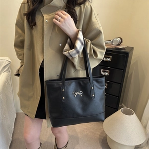 Minimalist black leather tote bag with gold bow detail, styled with a khaki trench coat