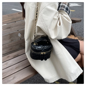 Detail of black quilted mini bucket bag with gold chain strap on model outdoors