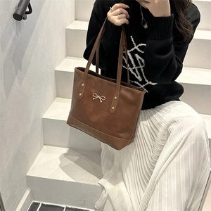 Brown leather tote bag with golden bow accent and dual handles on a white background
