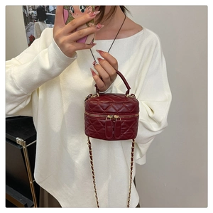 Detail of burgundy quilted leather crossbody bag with gold chain and top handle on model