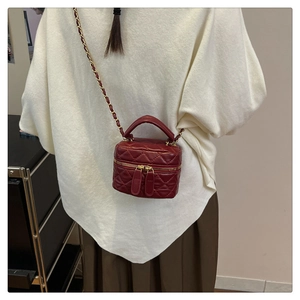 Detail of red quilted mini bucket bag with gold chain strap worn by a model