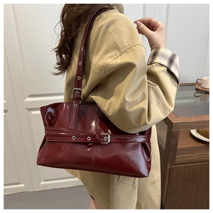 Detail of dark red patent leather tote bag with metallic buckle and slim shoulder strap