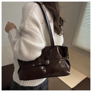 Gros plan du sac à bandoulière marron foncé brillant avec boucle sur un pull en maille