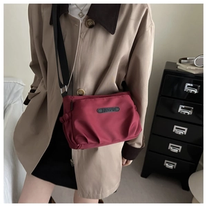 Detail of burgundy ruched crossbody bag with brand logo shown on model against home background