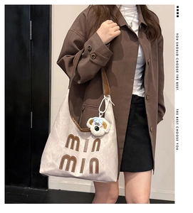 Detail of beige hobo tote bag with brown MIN MIN letters and plush dog charm