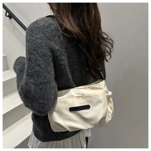 Close-up of minimalist cream nylon crossbody bag with pleated sides and thin black strap