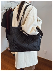 Woman in beige coat wearing a black quilted tote bag with stitched diamond pattern
