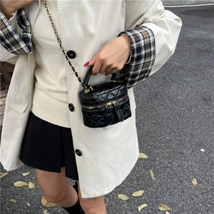 Mini quilted black bucket bag with chain strap and top handle worn with beige trench coat