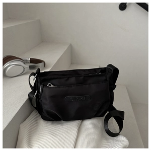 Close-up of black Oxford cloth crossbody bag featuring a zipper pocket and rubber brand logo