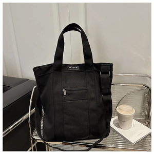 Macro detail of black canvas tote bag with adjustable strap and front zipper pocket