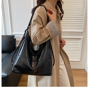 Detalle de un bolso tote grande negro en cuero brillante con una gabardina beige