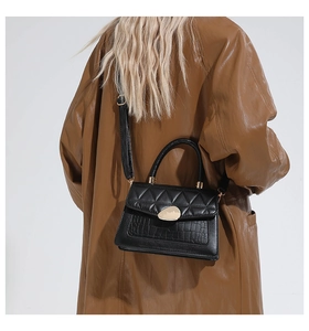 Détail d'un sac noir en similicuir avec boucle dorée porté sur un trench-coat en cuir brun