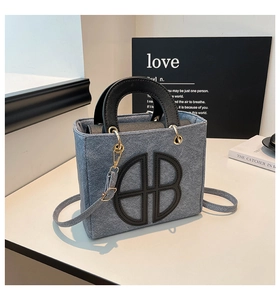 Dettaglio di borsa in denim azzurro con manici in pelle nera e decorazione circolare