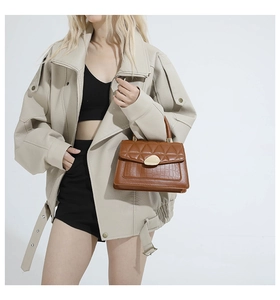 Détail d'un sac bandoulière en cuir marron matelassé avec texture croco et fermoir doré