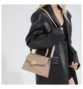 Gros plan d'un sac matelassé beige avec fermoir doré ovale et poignée de transport